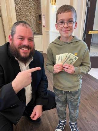 Chabad Hebrew School student Jacob Sentell of Monroe brought in $162 of his own savings to contribute to the program. He is pictured giving his donation to Rabbi Pesach Burston.